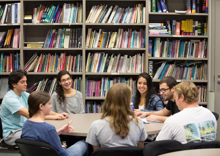 Students gather around a round table in front of a bookshelf.